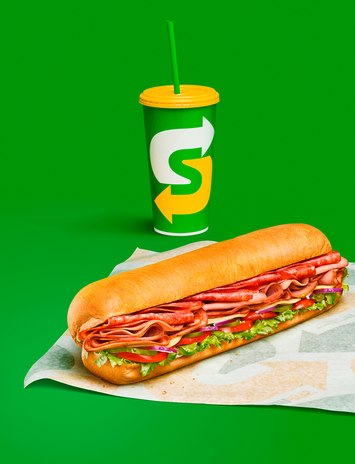 A subway sandwich and drink against a green background.